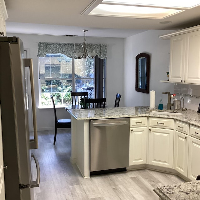 kitchen with light wood-type flooring, a peninsula, a sink, and appliances with stainless steel finishes