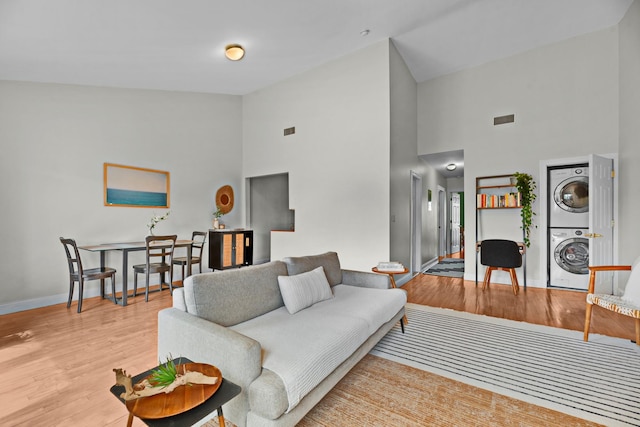 living area with visible vents, wood finished floors, stacked washer / dryer, baseboards, and high vaulted ceiling