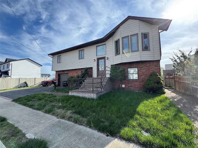 split foyer home featuring a garage, a front lawn, aphalt driveway, fence, and brick siding