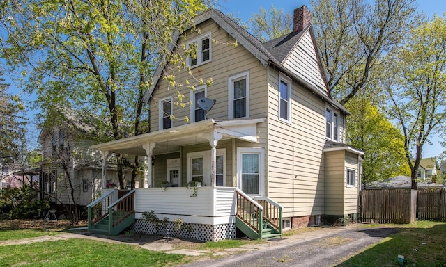 view of front of property featuring a porch, fence, a front yard, and a chimney