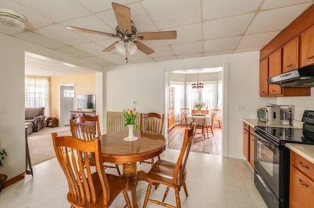 dining area featuring light floors, ceiling fan with notable chandelier, and a drop ceiling