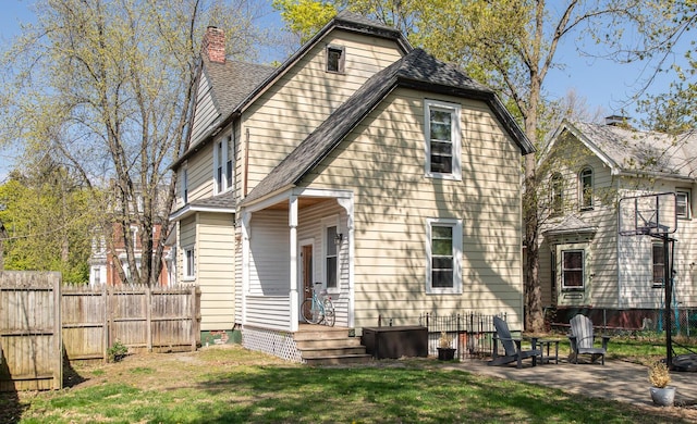 back of house with a chimney, roof with shingles, a lawn, fence, and a patio