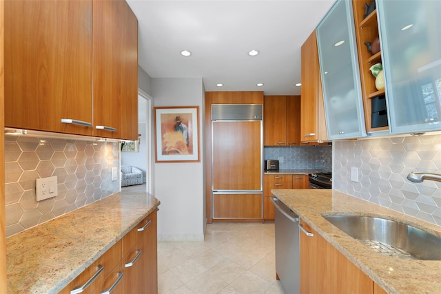 kitchen featuring backsplash, stainless steel dishwasher, a sink, paneled built in fridge, and brown cabinets