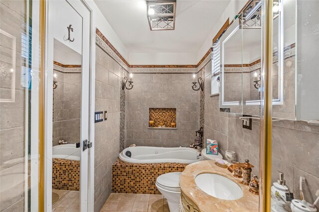 bathroom featuring tile patterned flooring, vanity, toilet, tile walls, and tiled tub