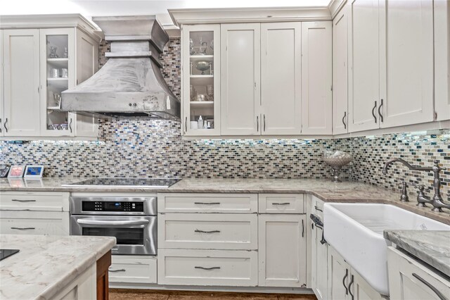 kitchen featuring oven, a sink, black electric cooktop, wall chimney exhaust hood, and tasteful backsplash