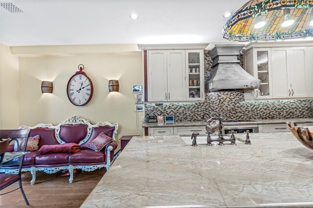 kitchen with decorative backsplash, light stone countertops, custom exhaust hood, and wood finished floors