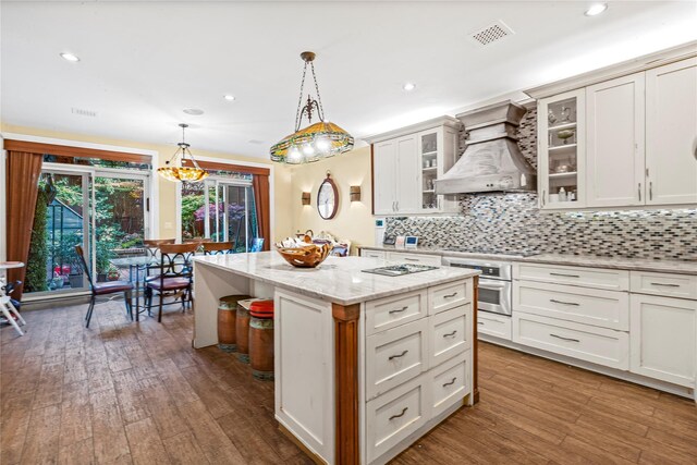 kitchen with visible vents, wood finished floors, oven, premium range hood, and a center island