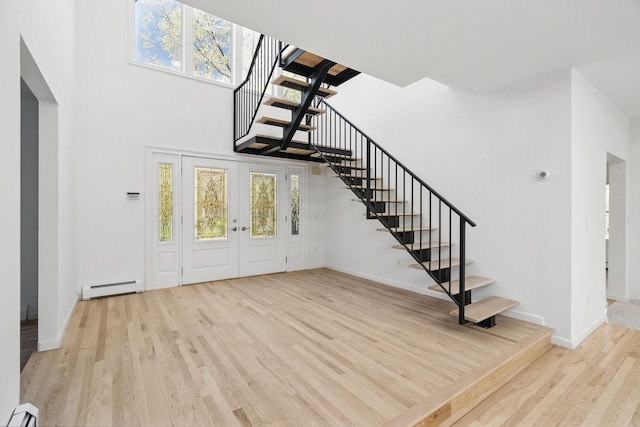 foyer entrance with baseboard heating, plenty of natural light, stairs, wood finished floors, and a baseboard radiator