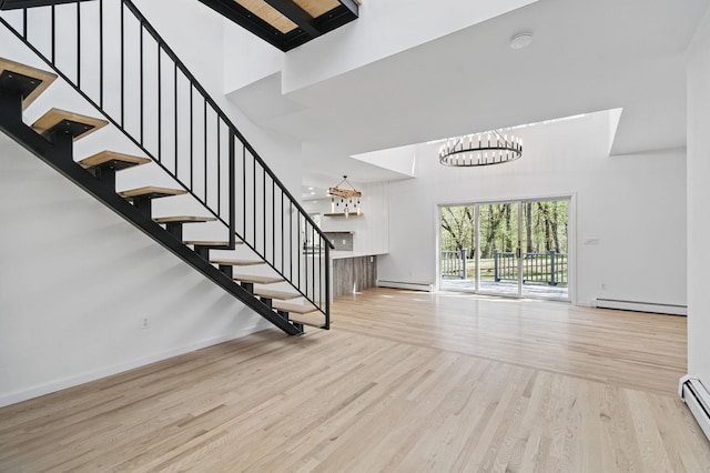 entrance foyer with stairs, a notable chandelier, a baseboard heating unit, and a towering ceiling