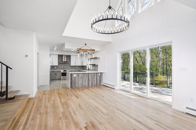 unfurnished living room with an inviting chandelier, a sink, stairs, a baseboard radiator, and light wood finished floors