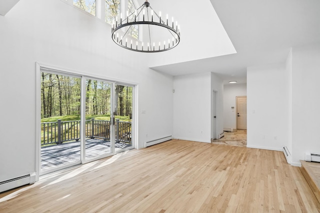 unfurnished living room featuring an inviting chandelier, a towering ceiling, wood finished floors, and baseboard heating