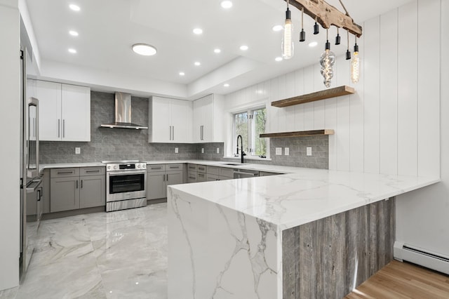 kitchen with decorative backsplash, baseboard heating, gray cabinets, wall chimney exhaust hood, and stainless steel appliances