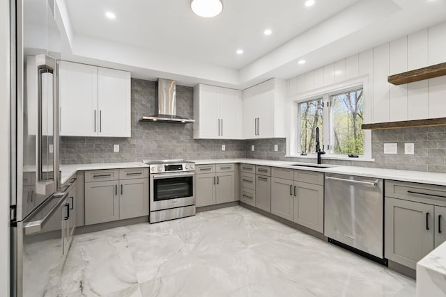 kitchen with open shelves, wall chimney exhaust hood, a sink, gray cabinetry, and stainless steel appliances