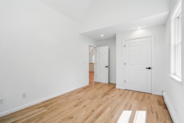 unfurnished bedroom featuring baseboards, a baseboard radiator, light wood-style flooring, and vaulted ceiling