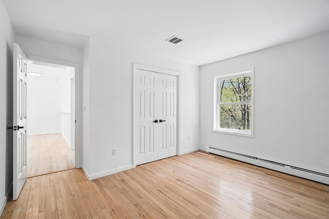 unfurnished bedroom featuring visible vents, baseboards, a closet, a baseboard heating unit, and light wood-style floors