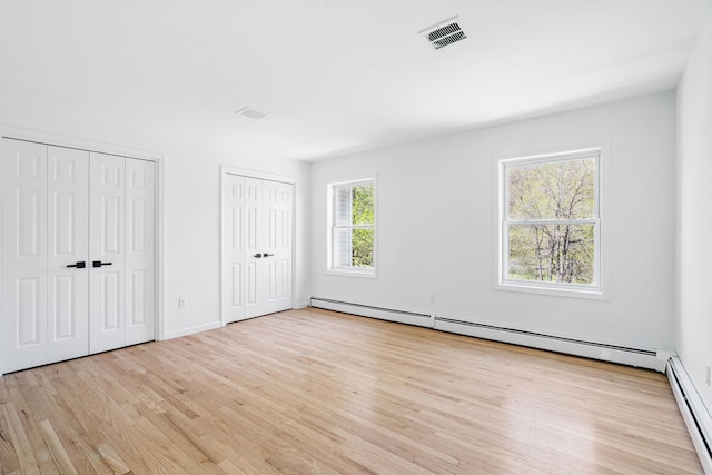unfurnished bedroom with visible vents, a baseboard heating unit, multiple closets, and wood finished floors