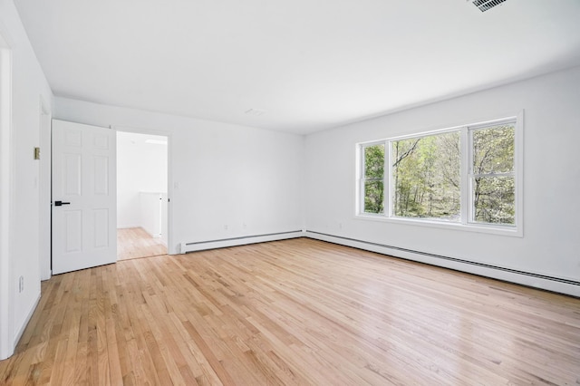 empty room with light wood-type flooring and a baseboard heating unit