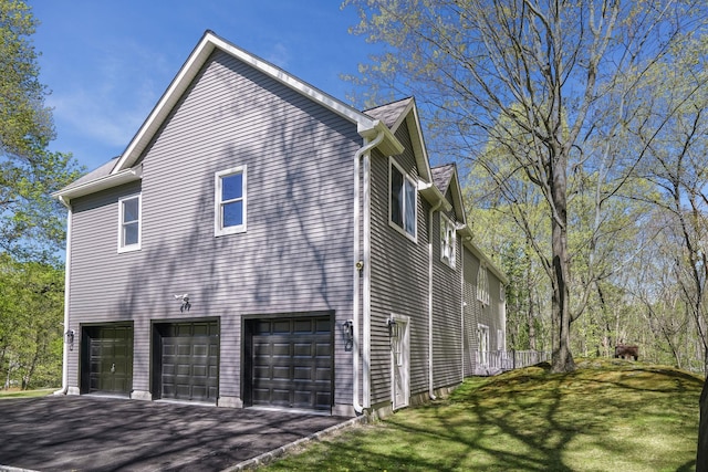 view of property exterior featuring a garage, a yard, and aphalt driveway