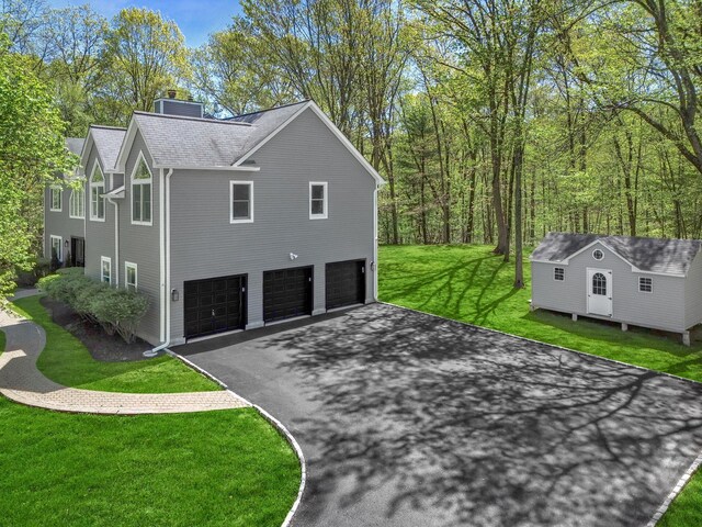 view of property exterior featuring a garage, aphalt driveway, a chimney, a lawn, and an outbuilding