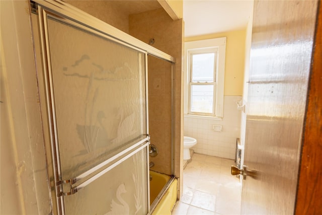 full bathroom with tile patterned flooring, wainscoting, toilet, tile walls, and bath / shower combo with glass door