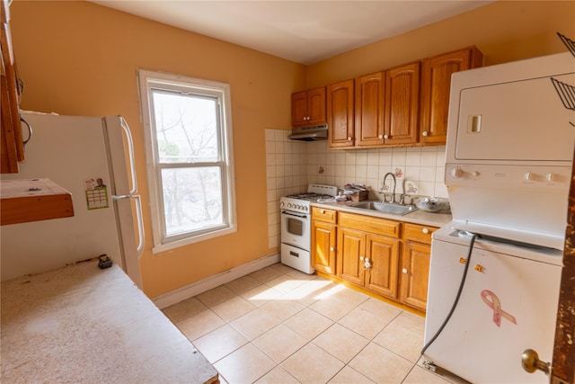 kitchen with stacked washer / drying machine, a sink, white appliances, light countertops, and under cabinet range hood