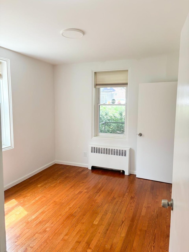 unfurnished room featuring baseboards, radiator, and light wood finished floors