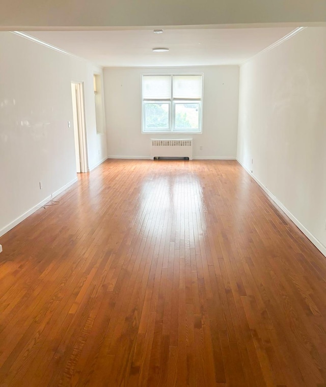 unfurnished room with baseboards, radiator, and hardwood / wood-style floors