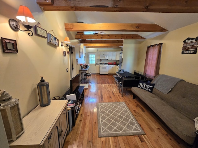 living area with a ceiling fan, wood-type flooring, and vaulted ceiling with beams