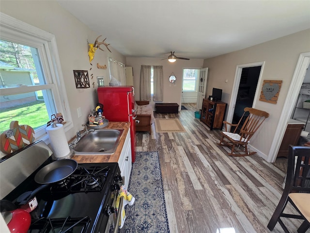 kitchen featuring wood finished floors, a sink, ceiling fan, black gas stove, and butcher block counters