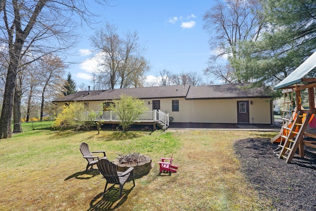 rear view of property with roof with shingles, a lawn, a deck, fence, and a fire pit