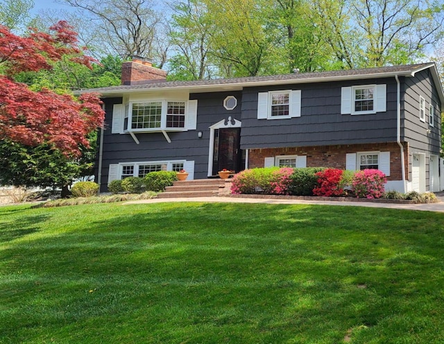 split foyer home featuring brick siding, a chimney, and a front yard