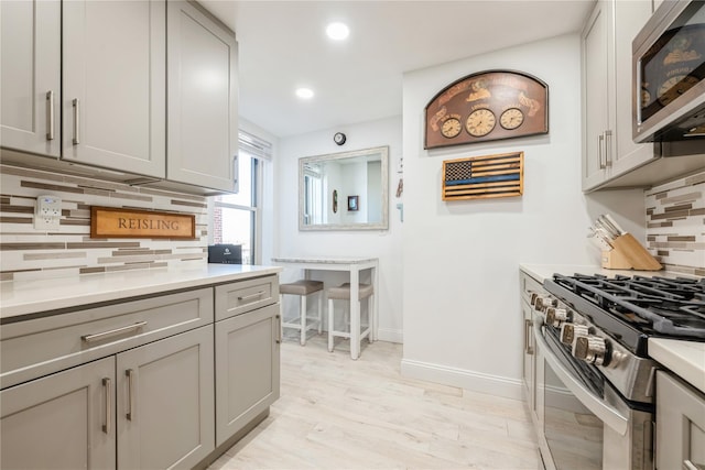 kitchen with decorative backsplash, gray cabinets, light countertops, baseboards, and stainless steel appliances