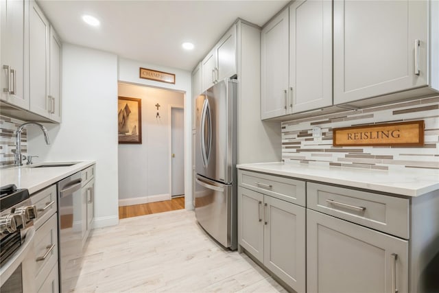 kitchen with stainless steel appliances, a sink, decorative backsplash, and gray cabinets