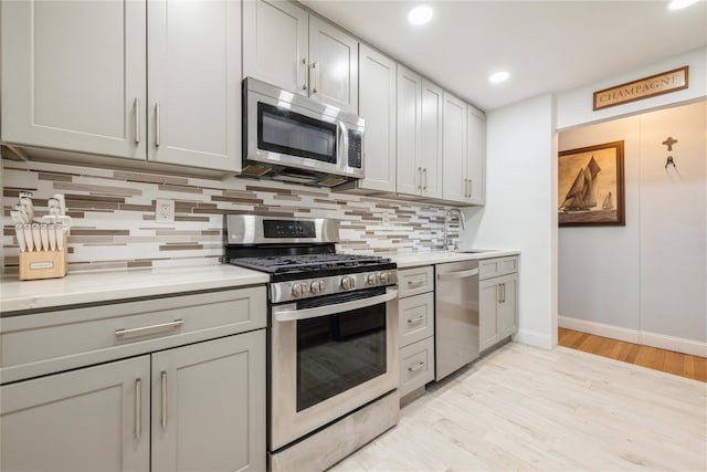 kitchen featuring light wood-style flooring, a sink, stainless steel appliances, light countertops, and tasteful backsplash
