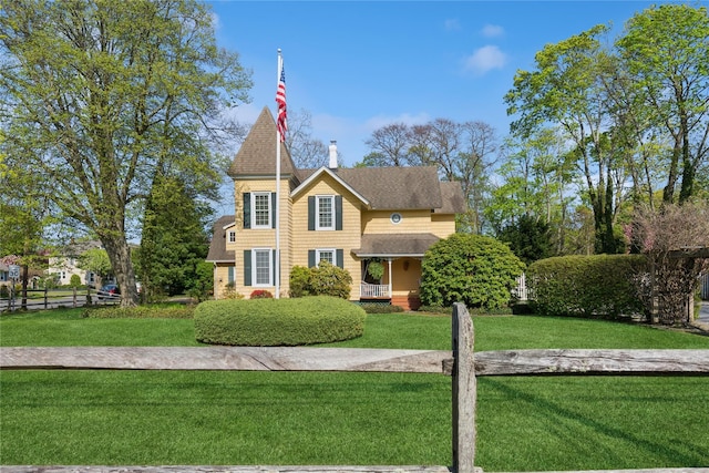 victorian-style house featuring a chimney, fence, a shingled roof, and a front lawn