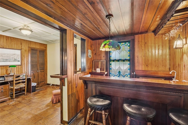 bar featuring pendant lighting, wood walls, wooden ceiling, baseboards, and indoor bar