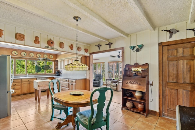 dining area with a ceiling fan, beam ceiling, light tile patterned flooring, and a textured ceiling