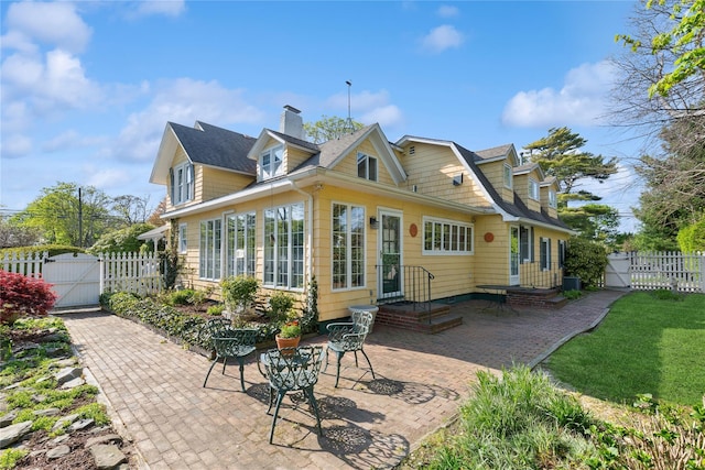 back of property with a patio, fence, a chimney, and a gate