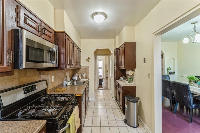 kitchen featuring backsplash, appliances with stainless steel finishes, arched walkways, baseboards, and light tile patterned flooring