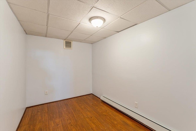 empty room featuring wood finished floors, visible vents, a paneled ceiling, and a baseboard radiator