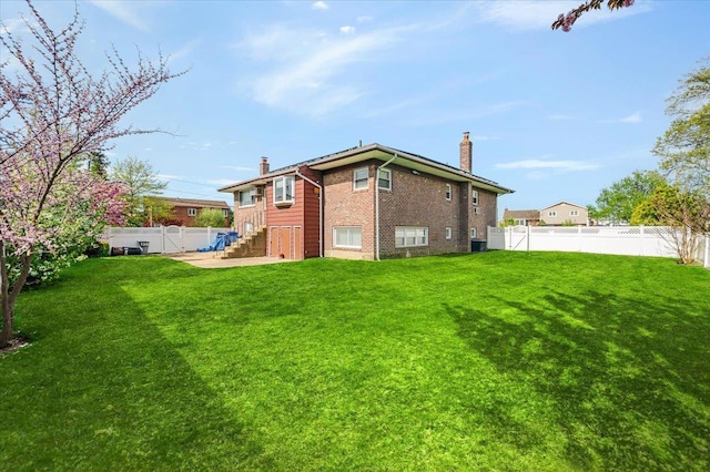 back of property with a yard, brick siding, a chimney, and a fenced backyard