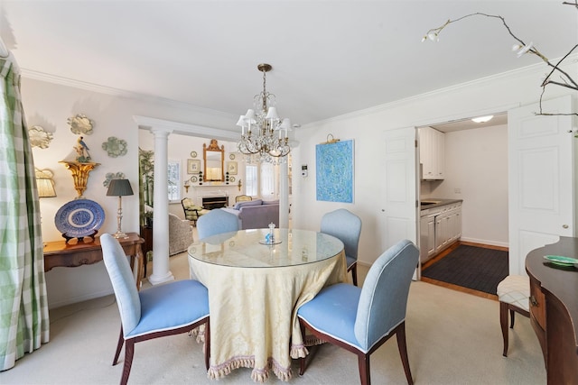 dining space featuring a fireplace, baseboards, a chandelier, ornamental molding, and ornate columns