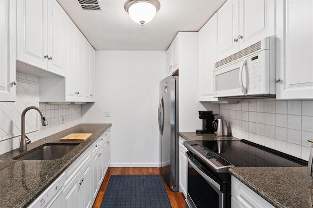 kitchen with a sink, white appliances, dark wood finished floors, decorative backsplash, and visible vents