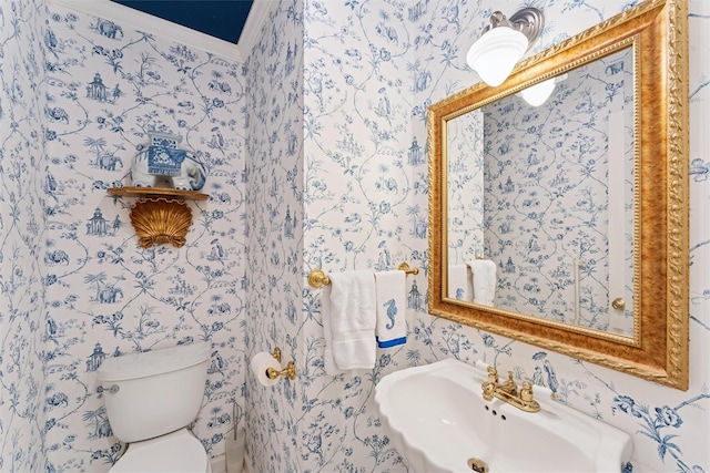 half bath with crown molding, toilet, wallpapered walls, and a sink