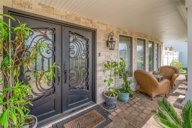 doorway to property with covered porch, french doors, and stone siding