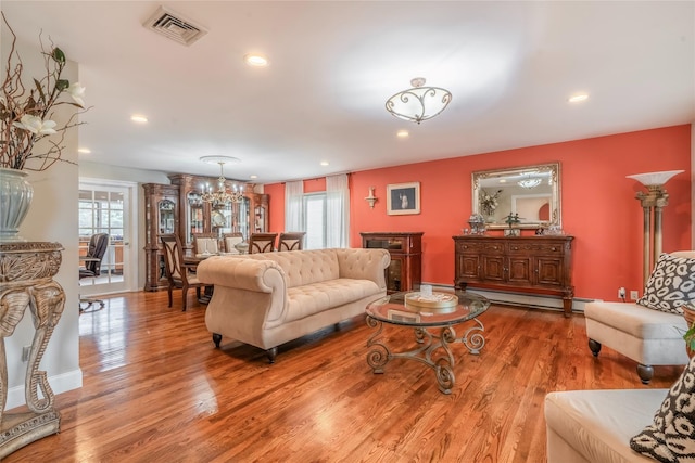 living area featuring baseboard heating, a notable chandelier, wood finished floors, and visible vents