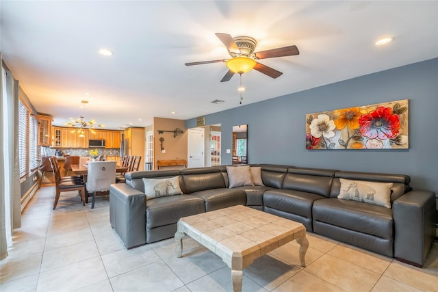 living room with a baseboard heating unit, a wealth of natural light, light tile patterned floors, and ceiling fan with notable chandelier
