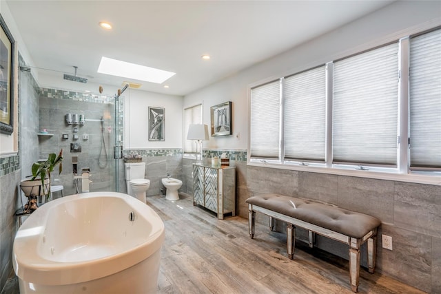 bathroom featuring a skylight, tile walls, a shower stall, wood finished floors, and a soaking tub