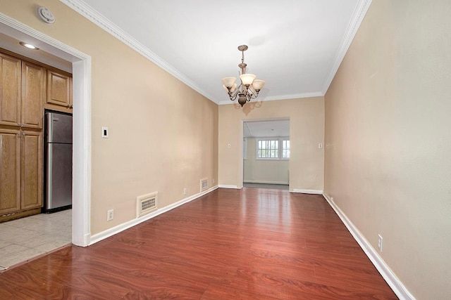 empty room featuring visible vents, wood finished floors, baseboards, an inviting chandelier, and ornamental molding