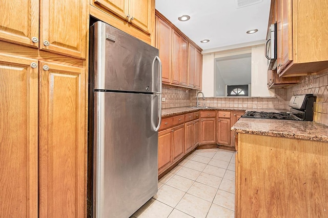 kitchen with light tile patterned flooring, tasteful backsplash, light stone counters, a sink, and stainless steel appliances